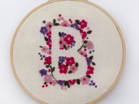 A flat needle felted floral design featuring a letter B on a fabric background. A pretty monogram artwork