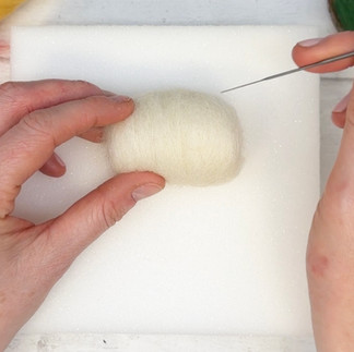 A bundle of cream core wool being poked by a felting needle.