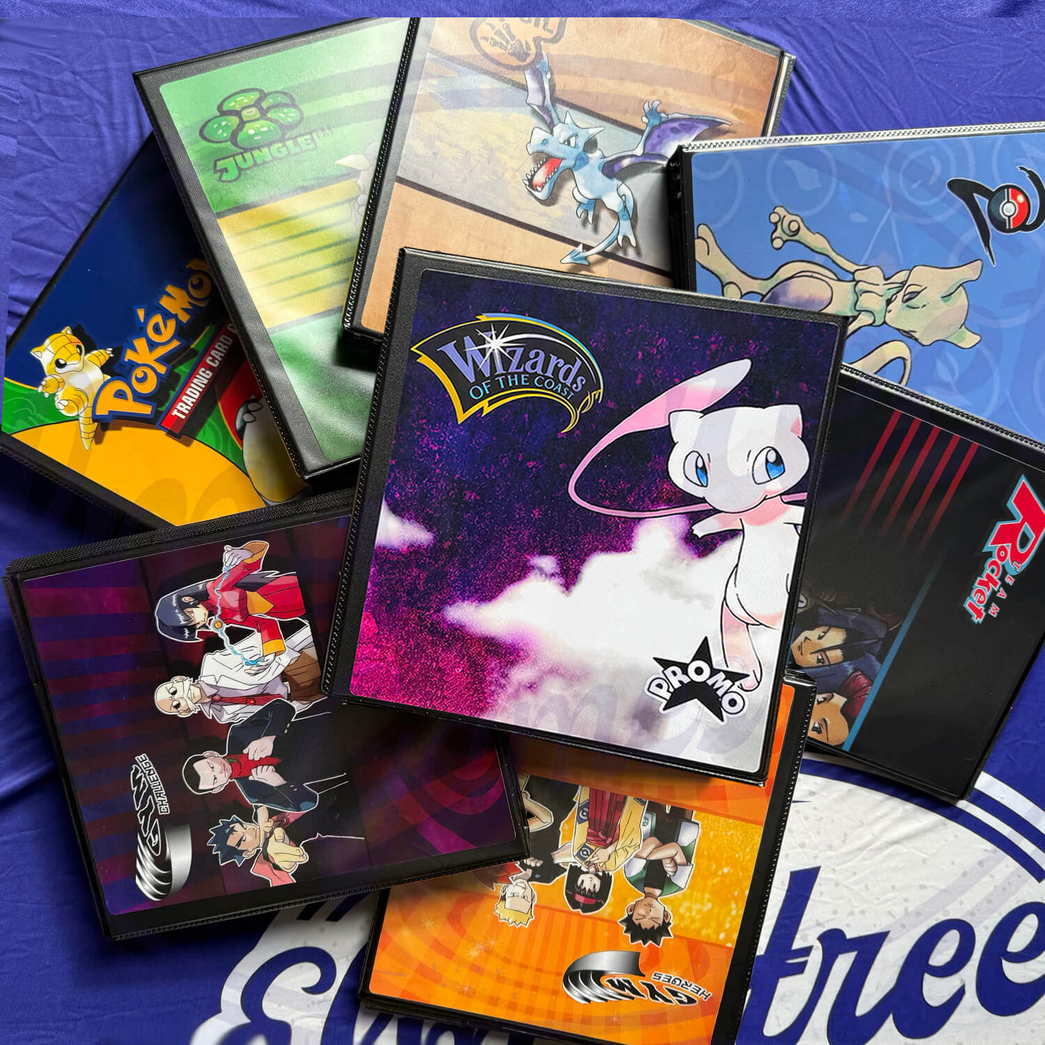 Collection of premium Pokémon card binders displayed on a vibrant background, featuring the Black Star Promo Pokémon binder in the center with a Mew design. Ideal for WOTC Black Star Promo card albums, Pikachu promo card organizers, and Wizards of the Coast promo binders.