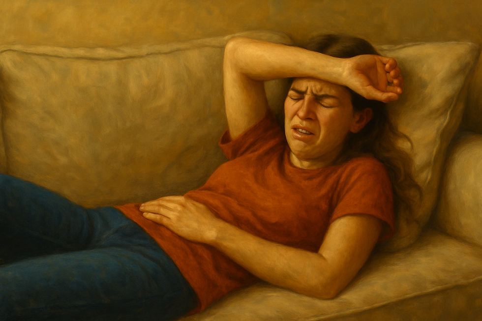 A girl wincing in pain and laying down on a couch with their arm across their forehead and eyes closed.