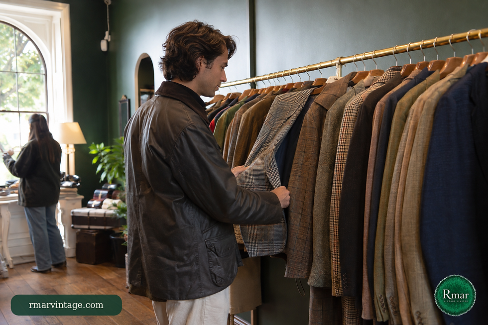 Customer browsing a brass rail of vintage jackets in a refined forest-green clothing shop.