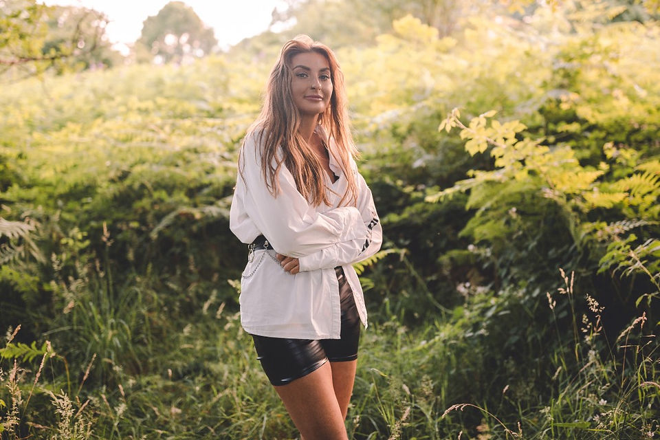 Brunette model posing for portrait photograph in a field at sunset wearing oversized white shirt and black shorts