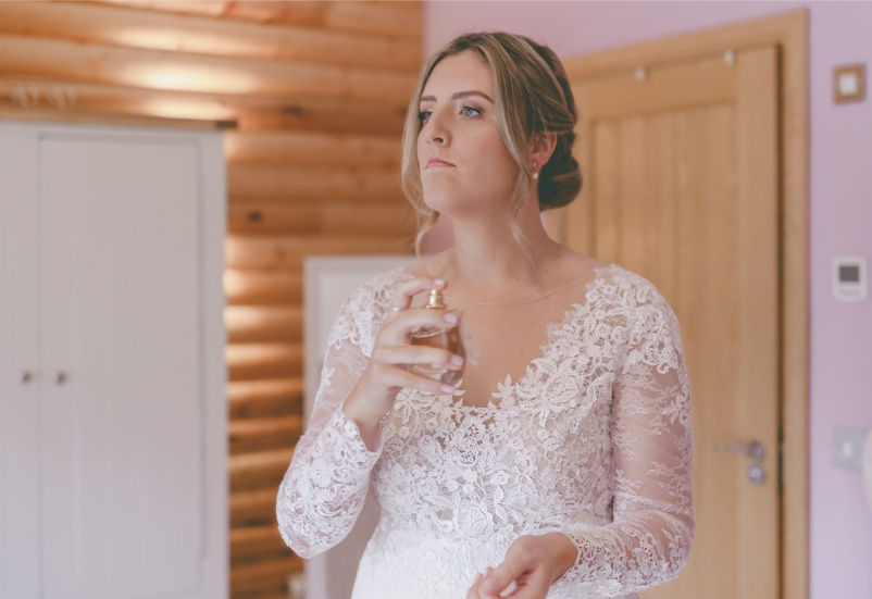 Bride spraying perfume on morning of her wedding at Canada Lodge & Lake in Cardiff, South Wales