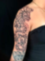 Illustrative blackwork dragon coiled through floral forms across the shoulder