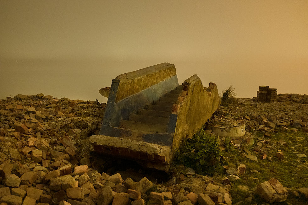 A broken staircase from a building by the eroded river bank at night.