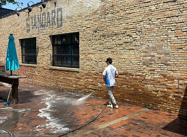 Hydros Power Washing technician cleaning the exterior of Standard Hall with professional equipment.