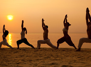 Yoga retreat group practicing poses on a remote Algarve beach at sunset.