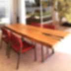 Mesa de jantar em madeira maciça com pés em inox, acompanhada de cadeiras vermelhas