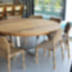 Mesa de jantar redonda em madeira maciça com pé central em inox, acompanhada de cadeiras de fibra trançada