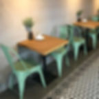 Pequena mesa de jantar em madeira maciça com pé central em aço carbono, acompanhada de cadeiras metálicas verdes