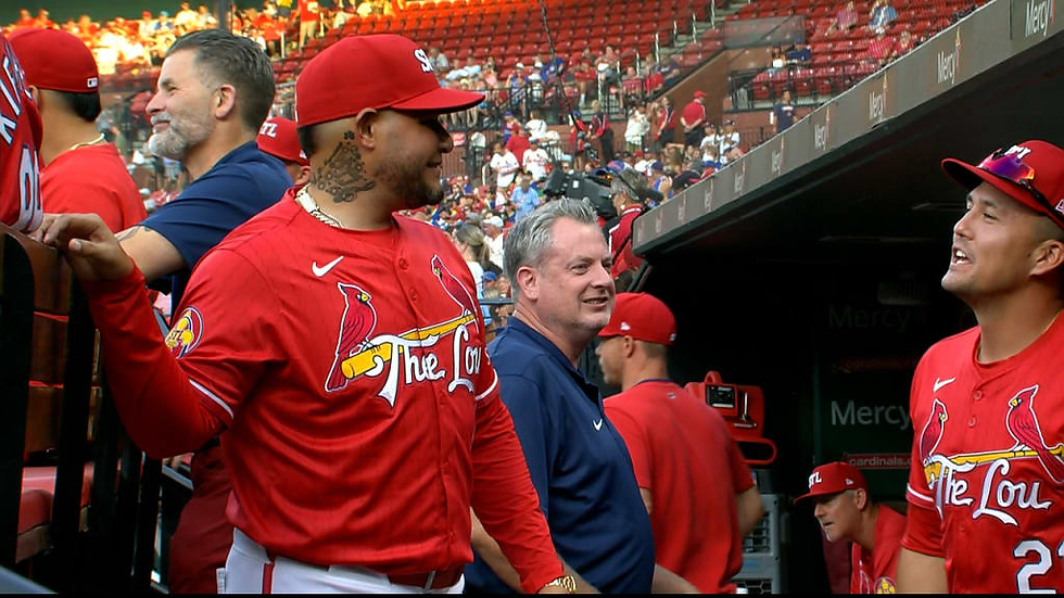 men, in a baseball dugout, wearing baseball uniforms, talk to each other