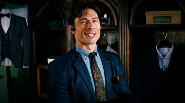 a man in a suit and tie has a bluetooth earphone in his ear and is grinning