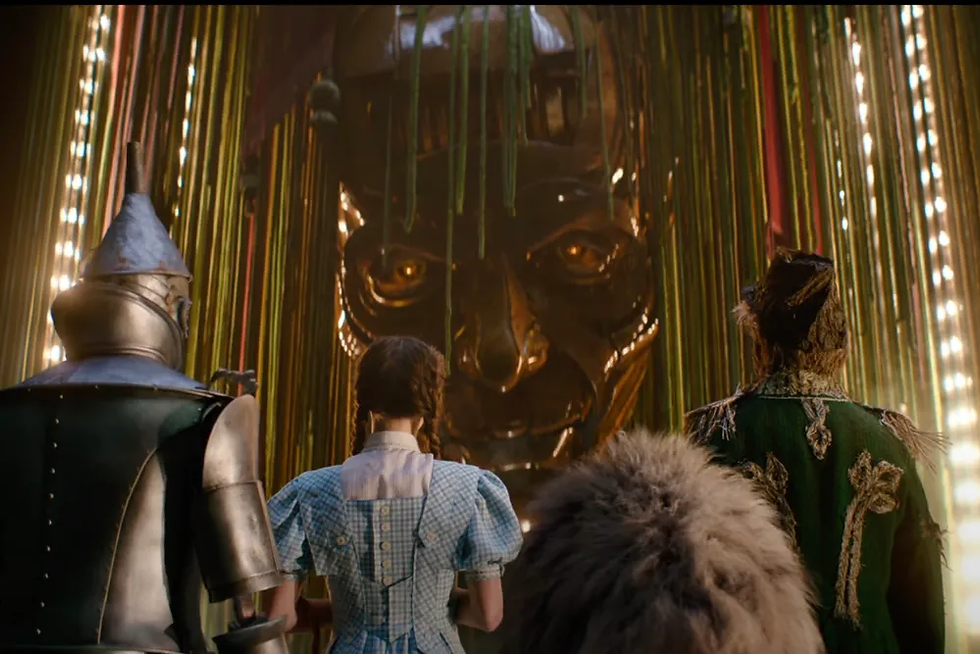 a tin man, girl, a lion, and a scarecrow are facing a large metallic face