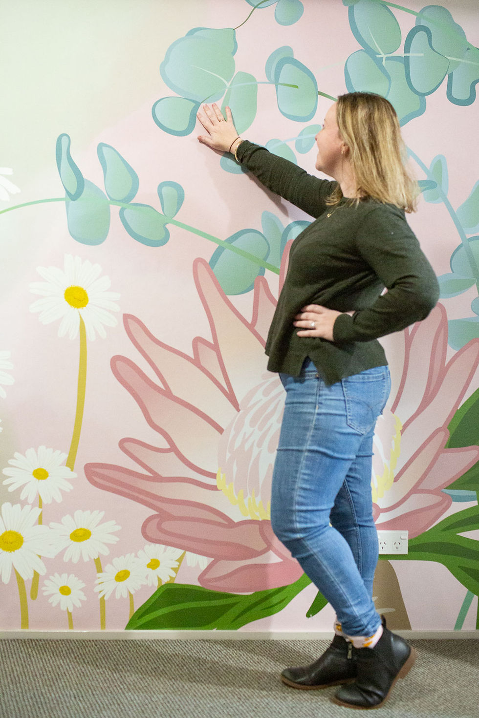 Wallpaper designer Kylie harber standing in front of her large scale wallpaper mural project featuring daisies, protea and silver dollar gum leaves.