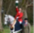 a rider in a red jacket on horseback, holding a large cup trophy having just won and cheering, being led by a judge.