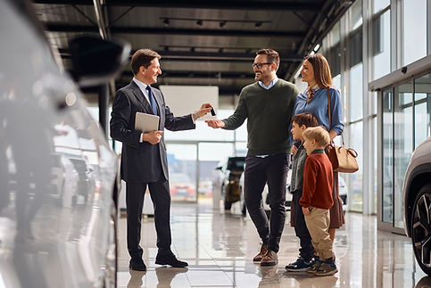 Happy salesman giving new car key to a family in auto salon .jpg