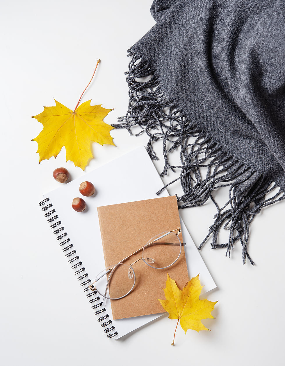 notepad glasses and yellow leaves with a scarf on white table