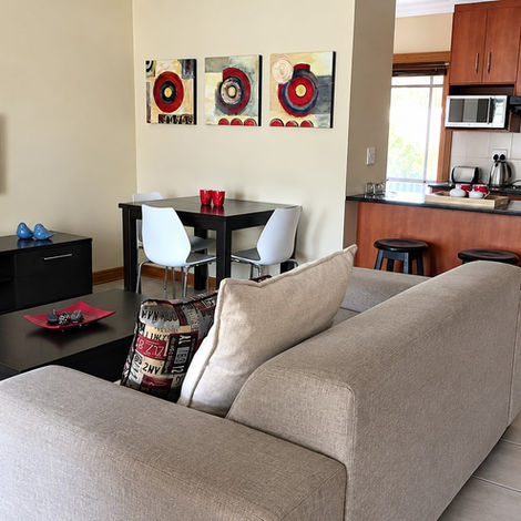 Open-plan townhouse living area with a grey sofa, round dining table and wood-finish kitchen cabinets.