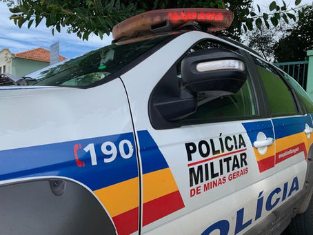 Uma viatura da Polícia Militar de Minas Gerais com o giroflex acionado, estacionada em uma via urbana.