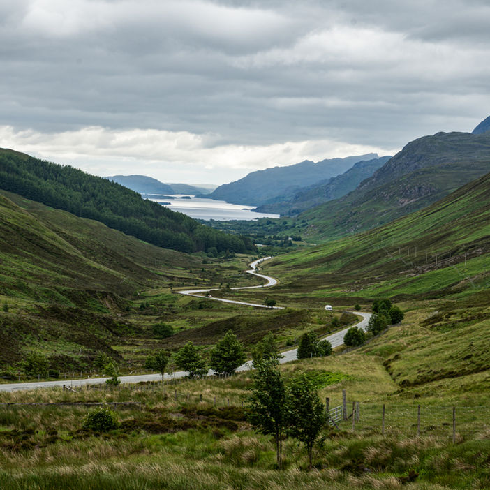 a lush green landscape with a winding road leading to the ocean