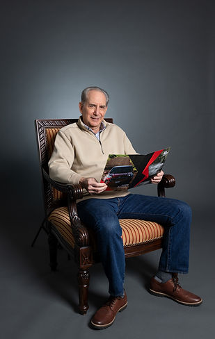 Old man posing nicely in a studio for professional dating profile photography with a magazine on vintage chair