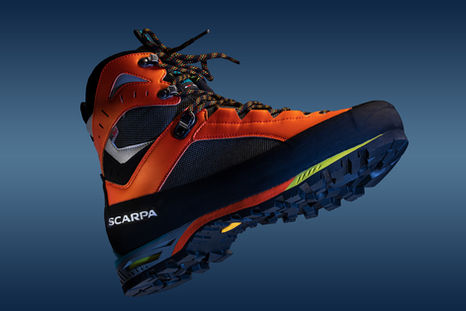 Bold orange Scarpa mountaineering boot with rugged sole on a gradient blue background, highlighting its superior durability and adventure-ready design.