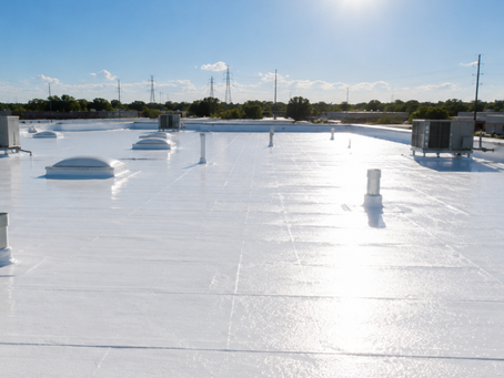 Bright white commercial rooftop with vents and HVAC units under a clear blue sky, sun glare reflecting across the surface.