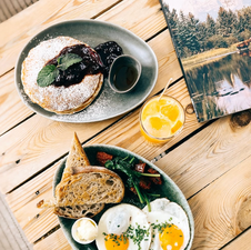 a dish of pancakes with jam, another dish with eggs and bread on a wooden table