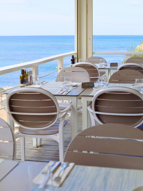 A restaurant white white chairs, grey tables and blue ocean in the background