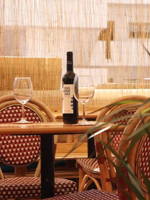A terrace table set with 2 glasses of wine and a red wine bottle. The atmosphere is casual in a late summer afternoon.