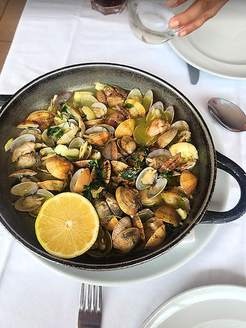 A frying pan filled with clams sitting in a garlic and lemon juice set on a white table top textile