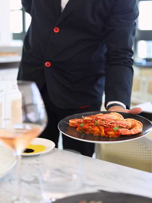 A waiter in a dark blue suit holding a plate of red jumbo shrimps at a Italian restaurant in Algarve