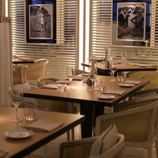 Elegant restaurant with neatly set tables and empty glasses. Framed black-and-white photos on walls. Warm lighting creates a cozy ambiance.