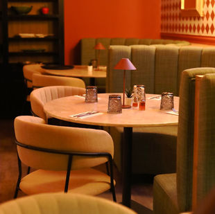 Cozy restaurant in Albufeira, Algarve with round tables, beige chairs, green booths, and red walls. Tv showing live sports games.