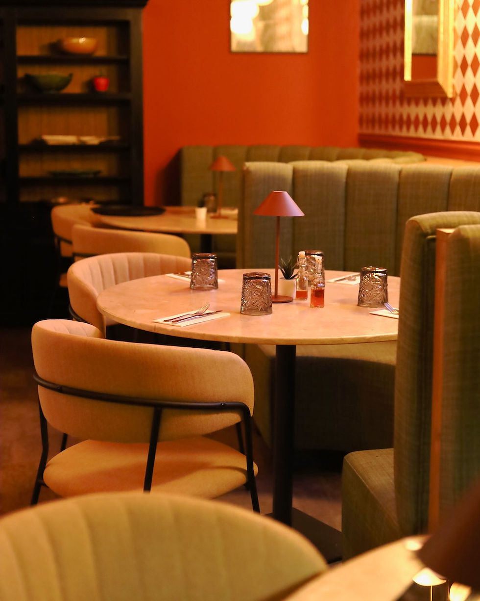 Cozy restaurant in Albufeira, Algarve with round tables, beige chairs, green booths, and red walls. Tv showing live sports games.