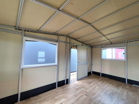 Innenraum des festen Vorzelts mit verlegtem Boden in Holzoptik, freiem Blick auf das Aluminiumgestänge, die Fenster und die geöffnete Schiebetür.