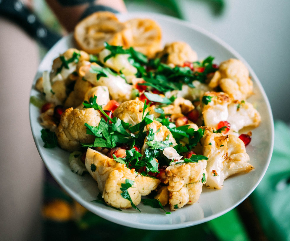 A chef holds a white plate full of roasted cauliflower and herbs