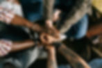 A diverse group of individuals uniting in solidarity with hands stacked together outdoors. Photo by Ivan S from Pexels.