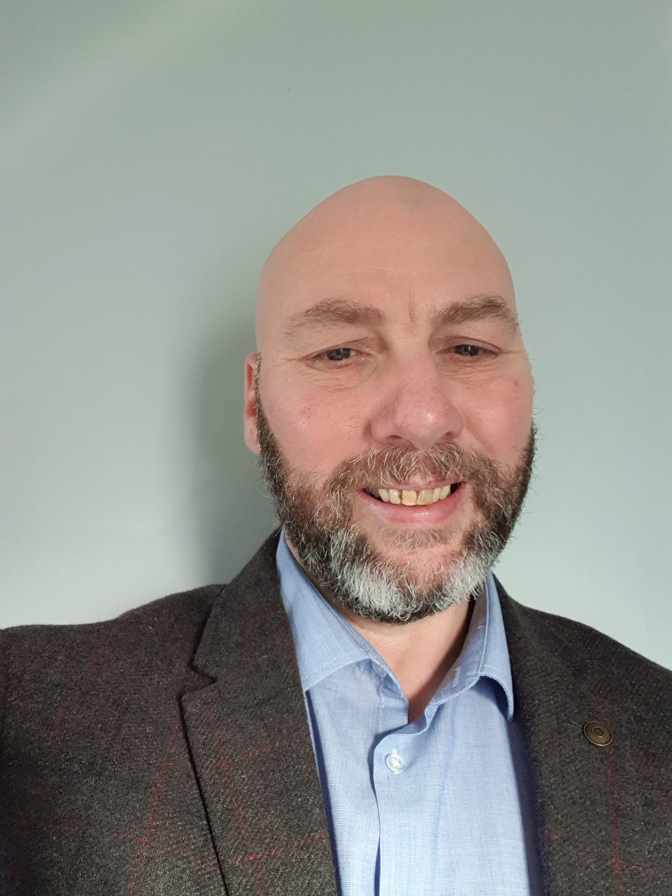 Man wears a blue shirt and dark jacket against a light gray background, creating a warm mood.