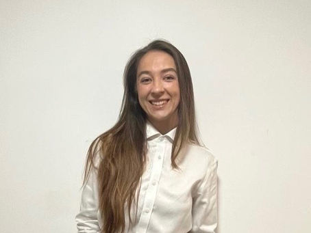 Young woman smiling, in a white shirt and black pants, stands against a plain white background.