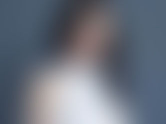 Young woman in a white top poses against a gray background. She has long hair with highlighted streaks and a subtle smile, conveying calmness.