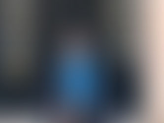 Person in a black coat and blue scarf stands smiling in front of a black door with "32" and "Thirty Two" visible, conveying a cheerful mood.