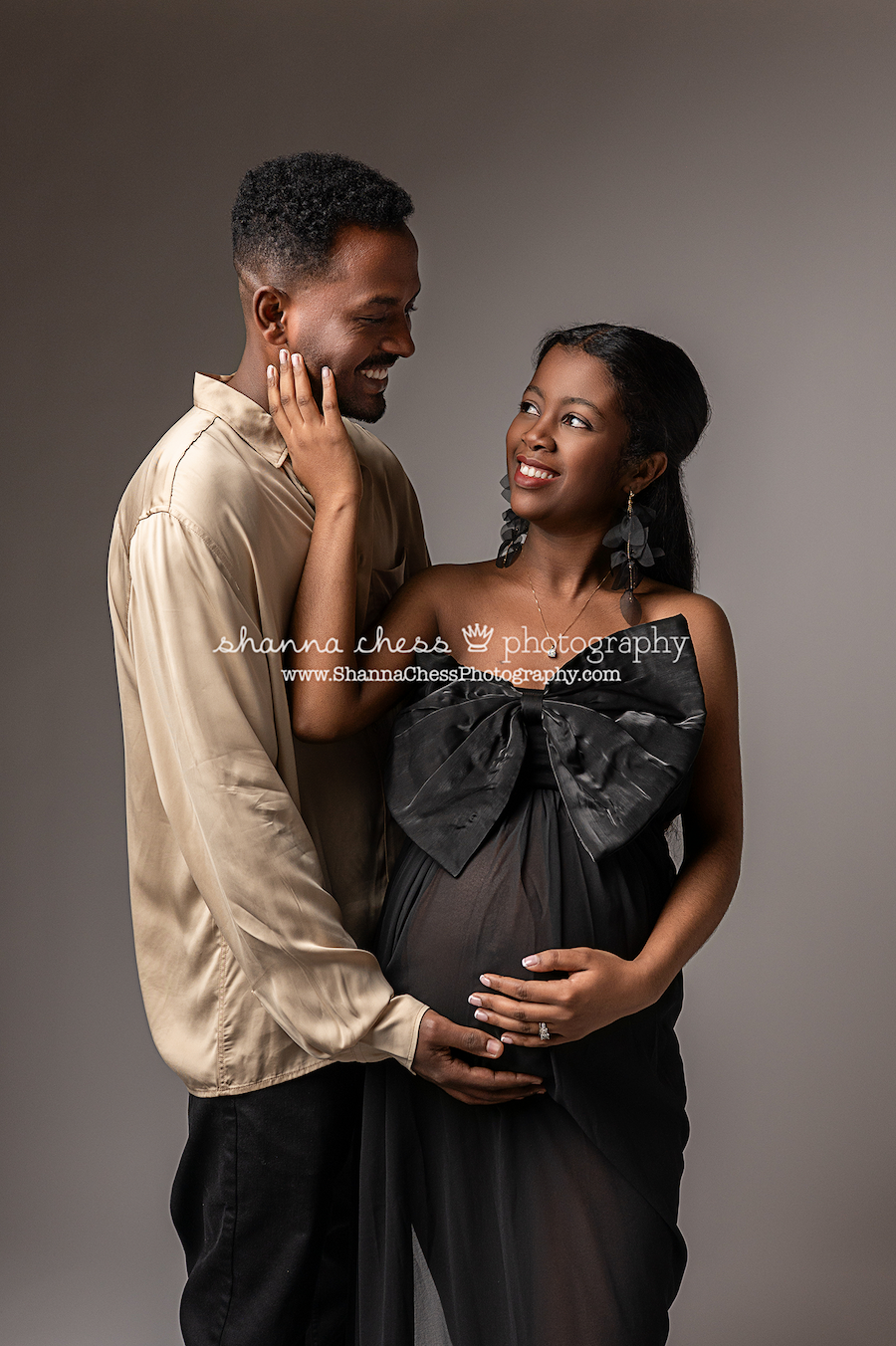 Black couple smiling at each other during their maternity portrait session in studio