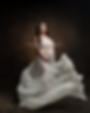 Woman cradles her pregnant belly as she poses in a flowing white maternity gown against a dark backdrop