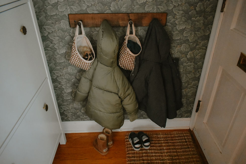 Coats and checkered bags on wall hooks, boots and slippers on wooden floor. Floral wallpaper, cozy entryway ambiance.