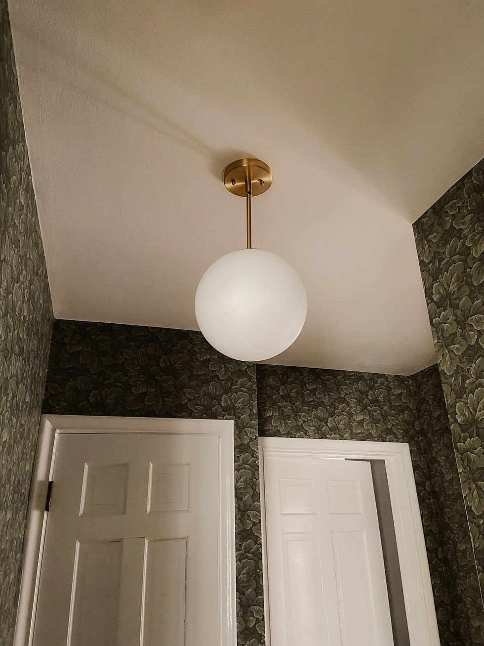 A white globe pendant light hangs from the ceiling in a hallway with floral wallpaper, framed by two white doors, creating a cozy mood.