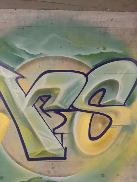 Ein Ausschnitt aus dem Graffiti-Kunstwerk in der Tiefgarage der Überbauung Hintersecki. Zu sehen sind die Buchstaben 'r' und 's' mit grünen Bergen im Hintergrund. Die Buchstaben haben eine präzise schwarze Outline, die ihnen Tiefe und Definition verleiht.