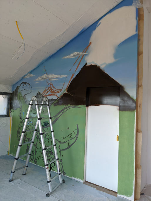 Das Anfangsstadium eines detailreichen Kunstwerks im Kinderzimmer, das einen prähistorischen Vulkan und Landschaft darstellt. Eine Leiter steht vor der Wand, auf der die ersten Umrisse und Farben des Kunstwerks zu sehen sind. Das Projekt wurde 2021 in Thurgau umgesetzt.