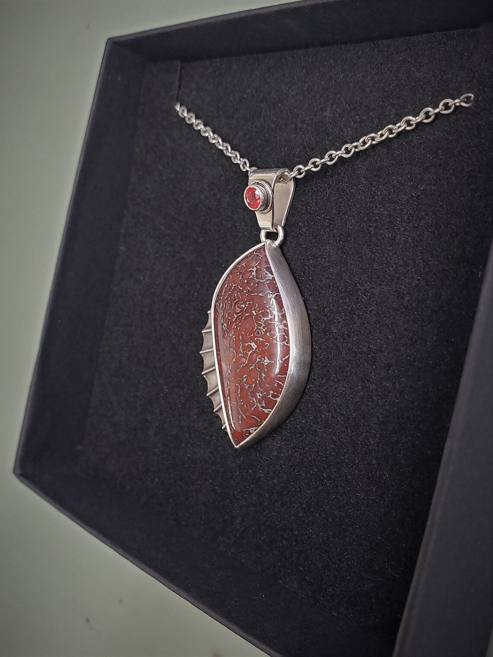 Thumbnail: Dinosaur bone pendant with orange sapphire accent stone in argentium silver shown against black background side view