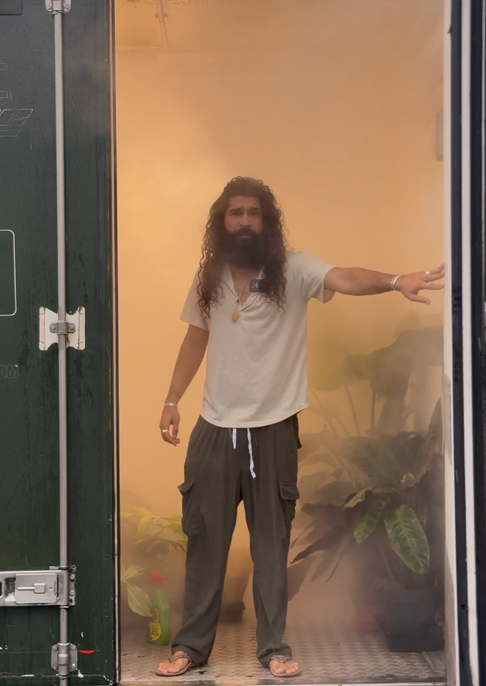 Bearded man with long hair opening the mist-filled doors of a plant container, revealing hundreds of rare new plant arrivals inside.